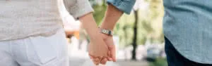 Two people holding hands outdoors in a park setting with blurred green trees in background