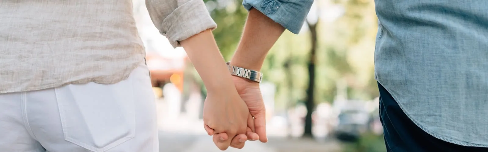 Two people holding hands outdoors in a park setting with blurred green trees in background