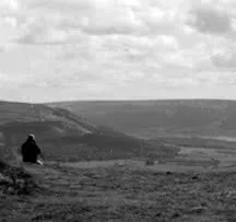 Person sitting alone on hillside overlooking vast valley landscape in black and white