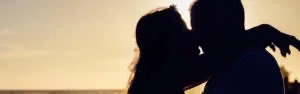 Silhouetted couple kissing at sunset with ocean horizon in warm golden light