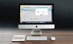Apple iMac desktop computer with wireless keyboard and mouse on wooden desk, displaying design software interface