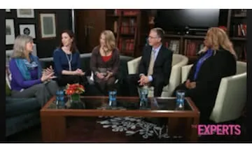 Five people sitting on beige chairs around a wooden table in a professional setting, appearing to be in conversation or panel discussion