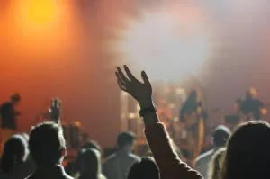 Silhouetted crowd with raised hands at concert or event with orange and yellow stage lighting