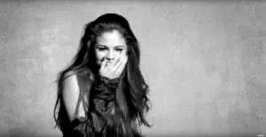 Black and white portrait of woman with long dark hair, hand near face, smiling against plain background