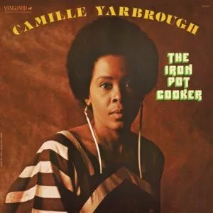Album cover featuring woman with afro hairstyle wearing striped shirt with headphones around neck