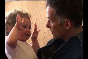 Adult and toddler face each other with hands raised in a playful interaction against a beige wall