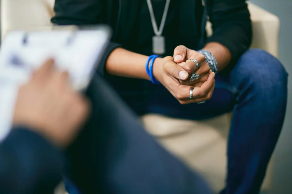 Person wearing blue bracelet and rings with hands clasped during therapy session