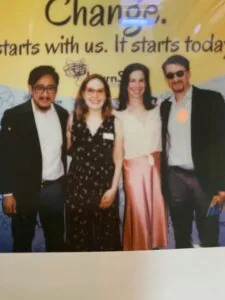 Four people standing together in front of a yellow and blue banner with text about change