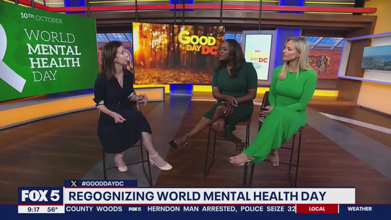 Three women sitting on a TV studio set discussing World Mental Health Day, with green signage visible behind them